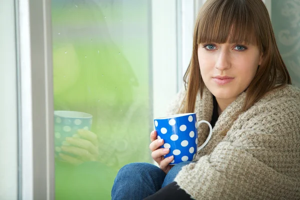 Jonge vrouw ontspannen door venster met kopje thee — Stockfoto