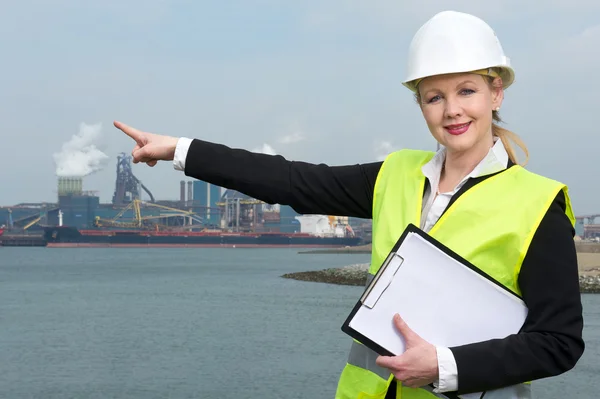 Supervisor perempuan dalam hardhat dan rompi pengaman menunjuk ke situs industri — Stok Foto