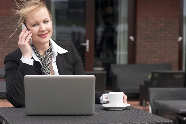 Affärskvinna på telefon utomhus med laptop och kopp kaffe — Stockfoto