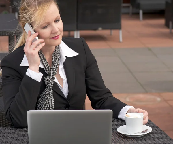 Zakenvrouw op een mobiele telefoon buiten zitten met laptop — Stockfoto