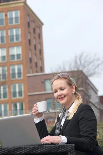 Usmívající se žena obchodní relaxaci s šálkem kávy a při pohledu na laptop obrazovky — Stock fotografie
