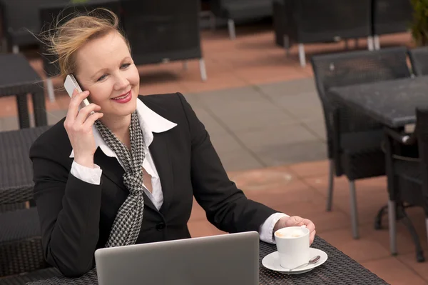Деловая женщина разговаривает по телефону во время отдыха на открытом воздухе с ноутбуком и чашкой кофе — стоковое фото