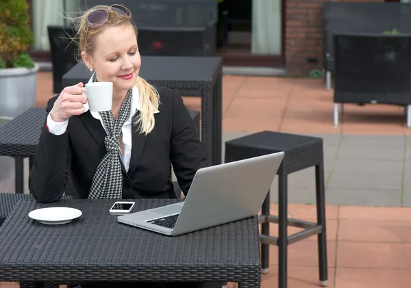 Glad affärskvinna kopplar av med en kopp kaffe och tittar på laptop skärm — Stockfoto