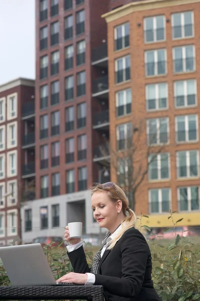 Affärskvinna arbeta utomhus med en kopp kaffe och tittar på laptop skärm — Stockfoto