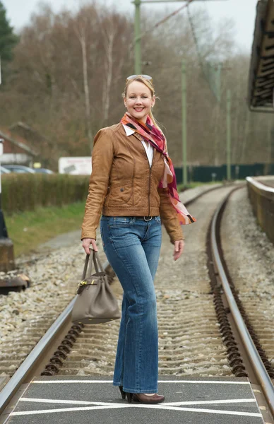 Портрет счастливой женщины, пересекающей железнодорожные пути с сумкой — стоковое фото