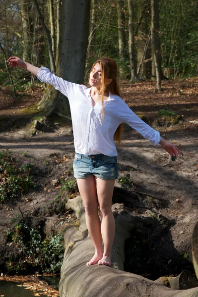 Mujer joven balanceándose en tronco de árbol con los brazos extendidos — Foto de Stock