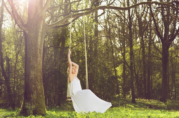 Portrait of a beautiful young bride sitting alone on swing outdoors — Stock Photo, Image
