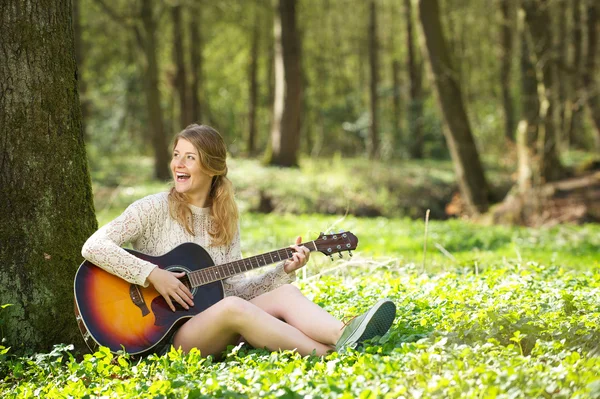 Портрет красивой молодой женщины, улыбающейся и играющей на гитаре на открытом воздухе — стоковое фото