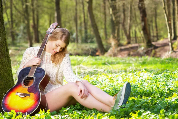 Güzel sarışın bir kadın ağacın altında gitar ile dinlendirici bir portresi — Stok fotoğraf