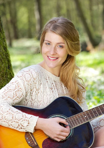 Портрет привлекательной молодой женщины, улыбающейся с гитарой на открытом воздухе — стоковое фото
