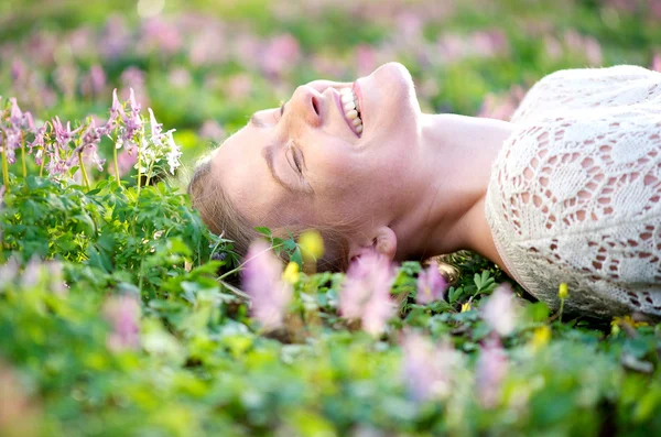 Sorridente giovane donna sdraiata in erba e fiori — Foto Stock