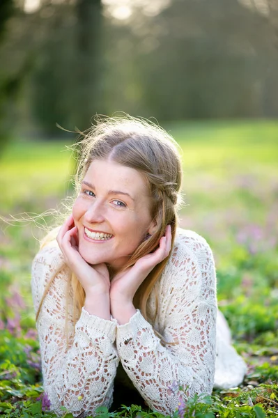 Jovem mulher sorrindo deitada na grama e flores — Fotografia de Stock