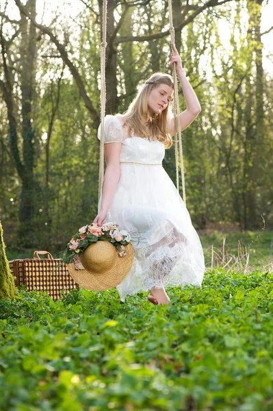 Jeune femme en robe blanche assise sur une balançoire à l'extérieur — Photo