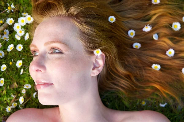 Retrato de uma bela mulher deitada na grama com flores no cabelo — Fotografia de Stock