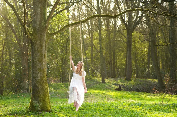 Ritratto di una sposa felice in abito da sposa bianco seduta su un giretto nel bosco — Foto Stock