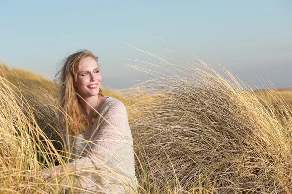 Giovane donna seduta tra le dune con erba lunga — Foto Stock
