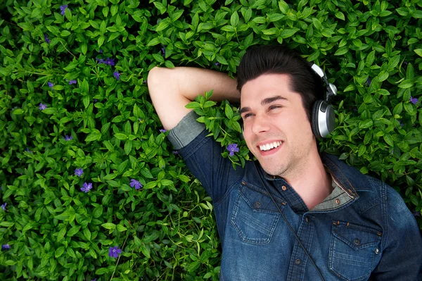Happy young man lying on grass, listening to music — Stock Photo, Image