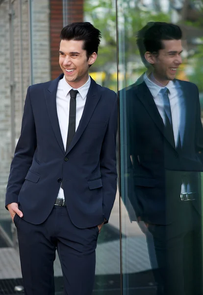 Happy businessman leaning against glass building — Stock Photo, Image