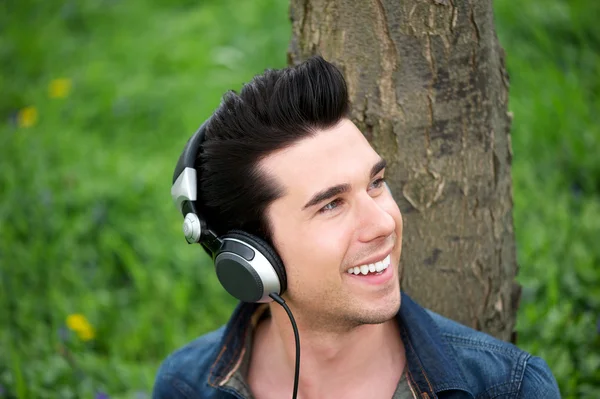 Attractive young man relaxing outdoors and listening to music on headphones — Stock Photo, Image