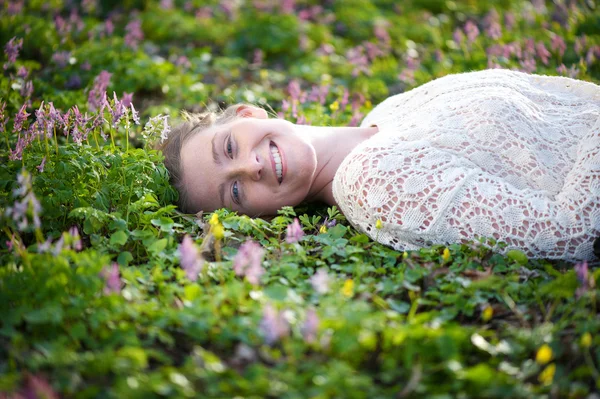 Vacker ung kvinna liggande på gräs med blommor — Stockfoto