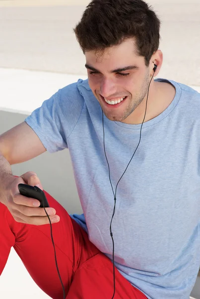 Portrett av en glad ung mann som lytter til musikk på mobilen sin – stockfoto