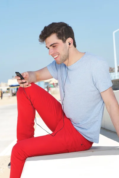 Portrét šťastný člověk poslouchá a při pohledu na mobilní telefon venku — Stock fotografie