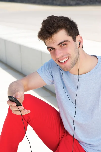 Giovane uomo sorridente e ascoltando il suo lettore mp3 all'aperto — Foto Stock