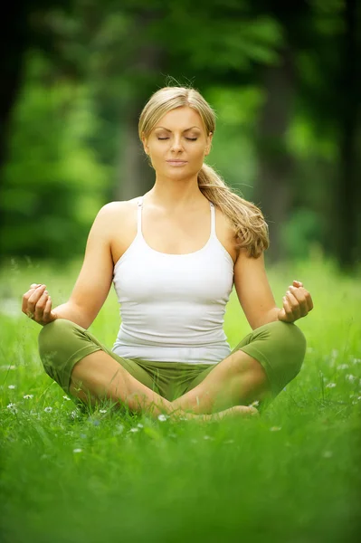 Красива молода жінка сидить в позі йоги в парку — стокове фото