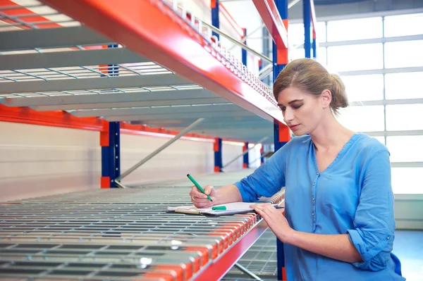 Businesswoman writing inventory on shelves in a warehouse — Stock Photo, Image