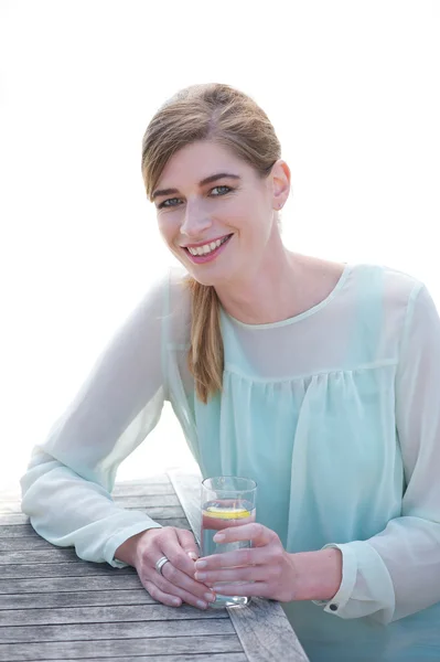 Junge Frau lächelt und genießt einen frischen Drink in einem Restaurant im Freien — Stockfoto