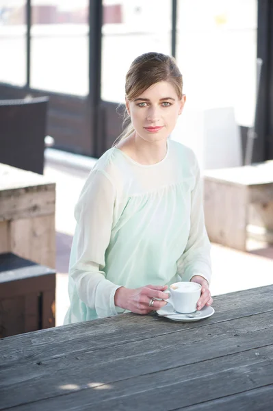 Bir fincan kahve ile bir masada oturan genç kadın — Stok fotoğraf