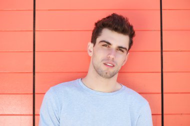 Turuncu duvara yaslanmış çekici bir genç adam