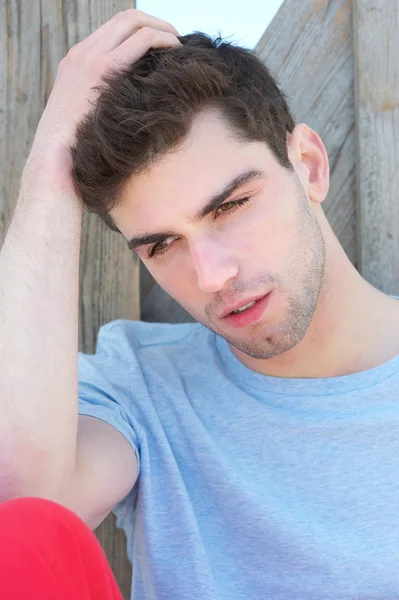 Young man sitting outdoors with hand in hair — Stock Photo, Image