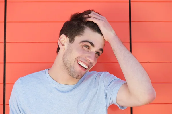 Atrakcyjny młody człowiek uśmiechający się ręką w włosy — Zdjęcie stockowe