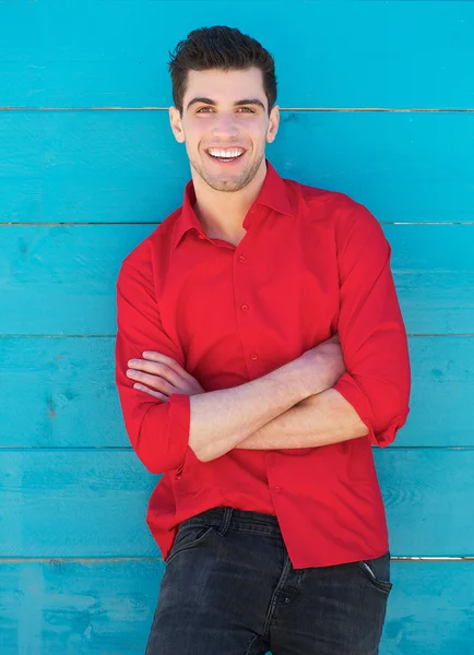 Mladý muž s úsměvem venku proti modré zdi — Stock fotografie