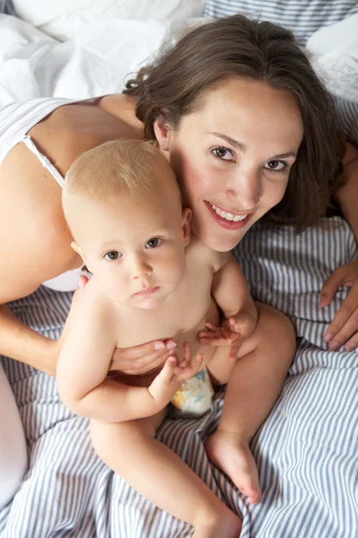 Schöne Frau hält Baby im Bett — Stockfoto