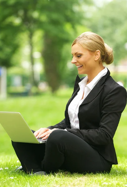 Glad affärskvinna som sitter på gräset med laptop — ストック写真