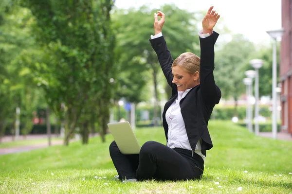 Businesswoman sitting outdoors with laptop and arms up in celebration — Stock Photo, Image