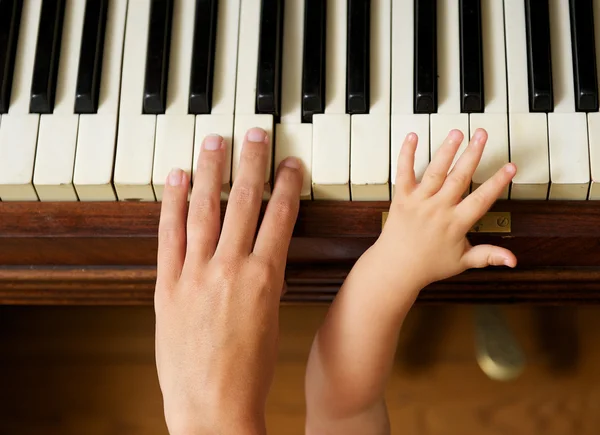 Adult hand playing piano with baby hand — Stock Photo, Image