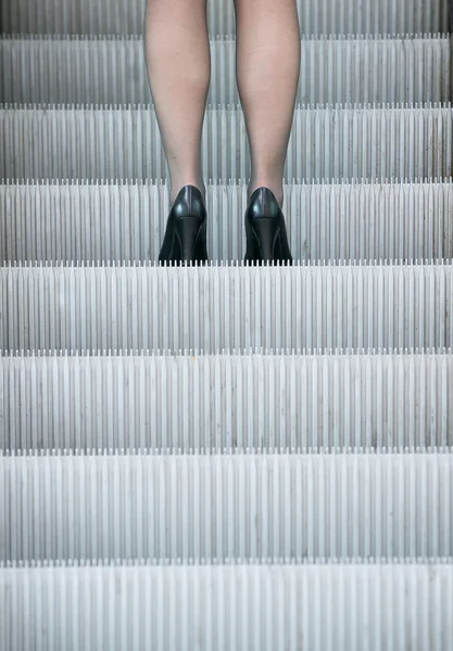 Mujer de negocios en tacones altos de pie en escaleras mecánicas — Foto de Stock