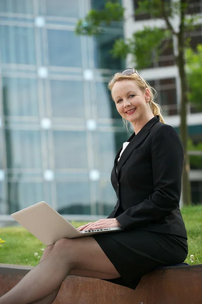 Affärskvinna sitter utomhus och ler med laptop — Stockfoto