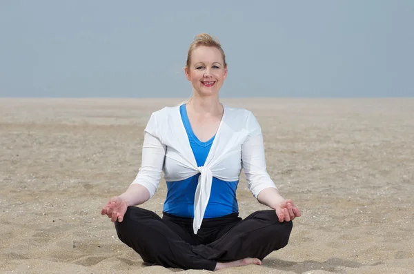 Kobieta siedzi w pozycji jogi na plaży — Zdjęcie stockowe