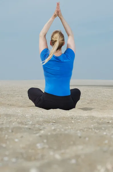 Mujer sentada en la playa con las manos en alto en posición de yoga — Foto de Stock