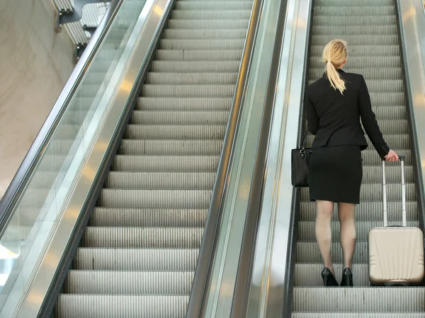 Geschäftsfrau steht mit Reisetasche auf Rolltreppe — Stockfoto