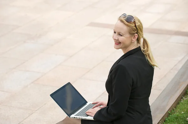 Businesswoman smiling outdoors with laptop — Stock Photo, Image