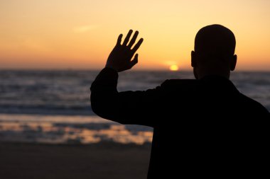 Male silhouette waving at sunset at the beach clipart