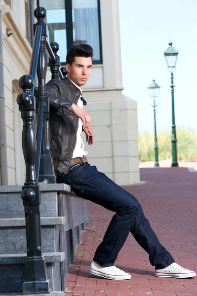 Männermode-Model in Lederjacke sitzt draußen — Stockfoto