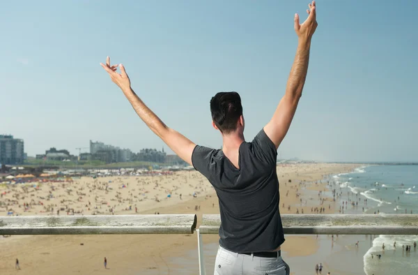 Hombre con las manos levantadas con vistas a la playa con gente —  Fotos de Stock