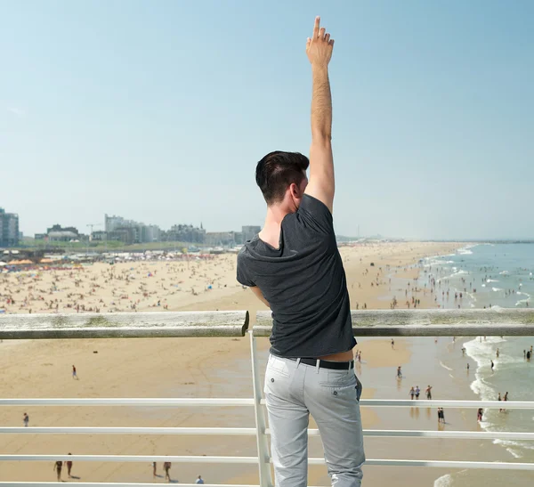 Young man with hand raised pointing up, beach in background — Stock Photo, Image