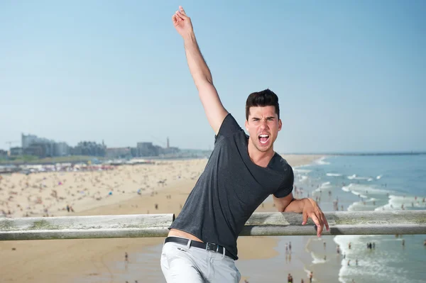 Jovem animado com a mão levantada na praia — Fotografia de Stock